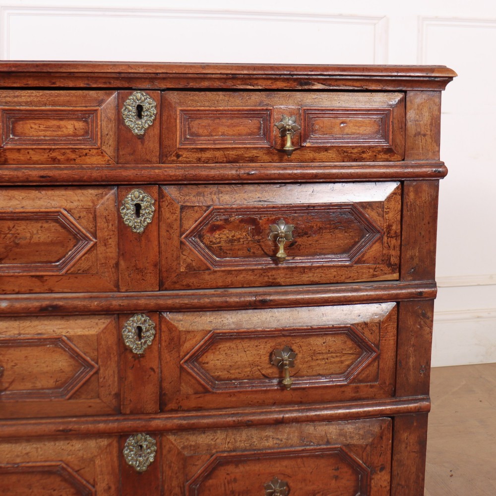An eighteenth-century oak chest of drawers featuring geometric panelled drawer fronts, brass drop handles, brass escutcheons, and bracket feet. View III