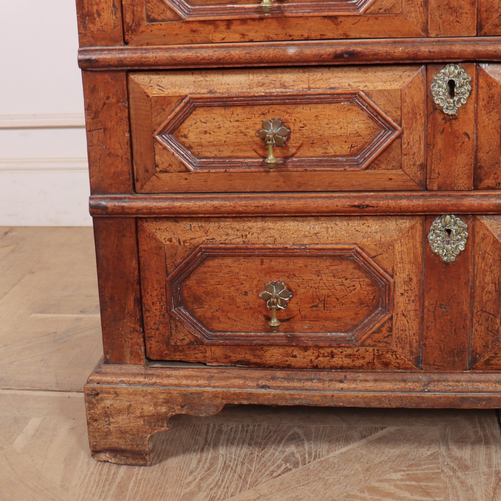 An eighteenth-century oak chest of drawers featuring geometric panelled drawer fronts, brass drop handles, brass escutcheons, and bracket feet. View IV