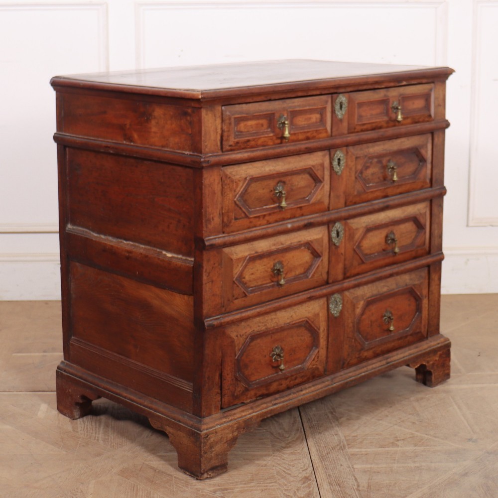 An eighteenth-century oak chest of drawers featuring geometric panelled drawer fronts, brass drop handles, brass escutcheons, and bracket feet. View VII
