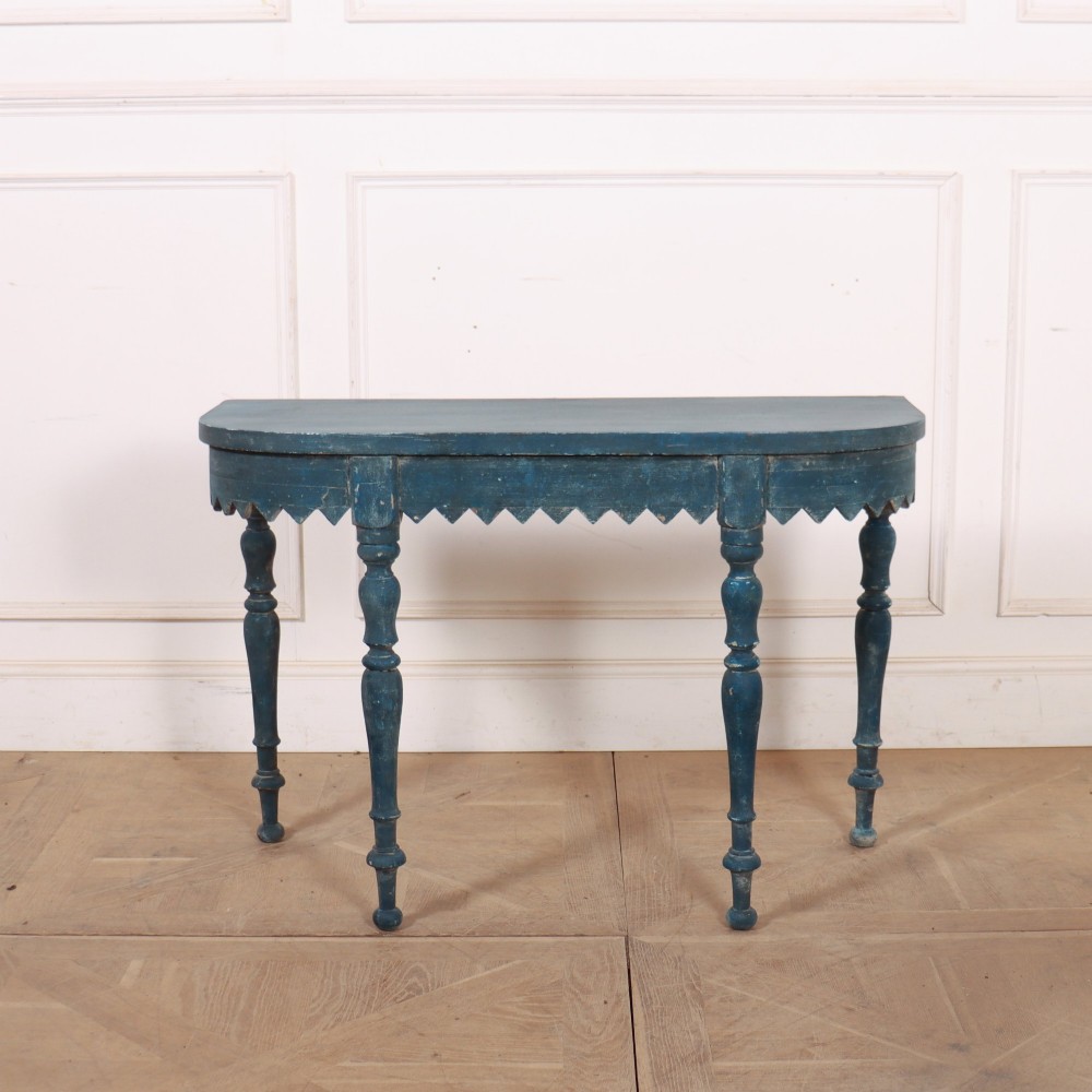 A blue painted wooden console table featuring rounded bow ends, a scalloped apron, and four turned legs.