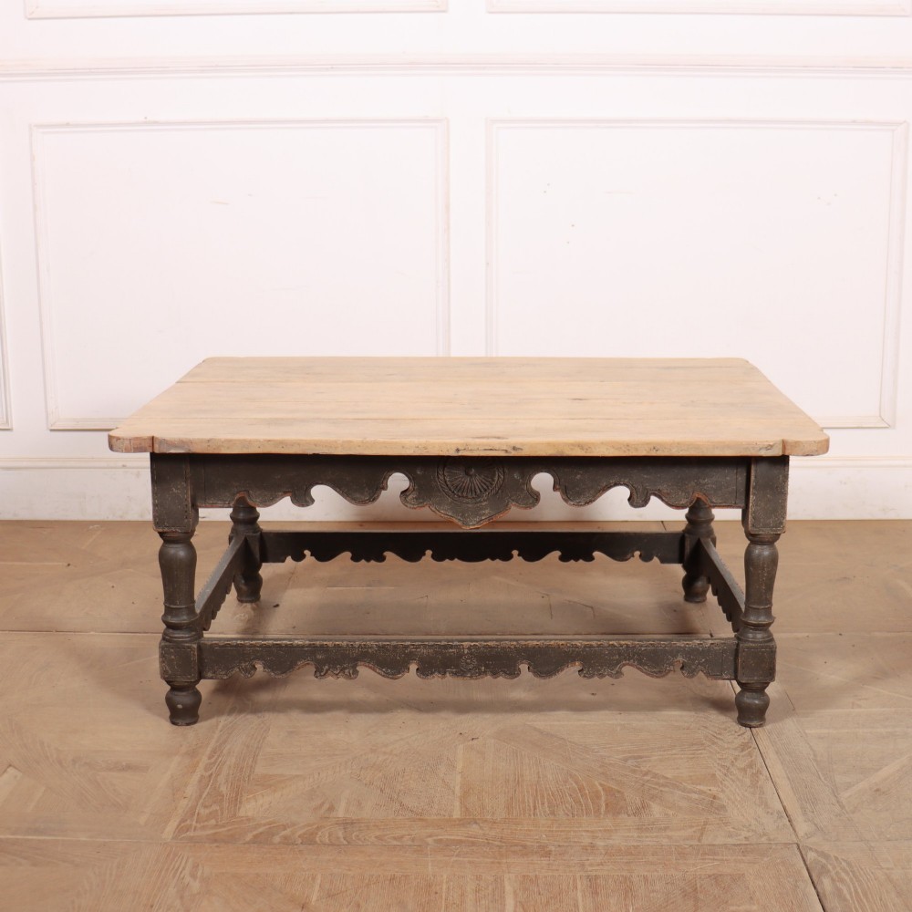 A low rectangular coffee table with a scrubbed pine top and dark painted frame featuring scalloped aprons, a carved shell motif, and turned legs.