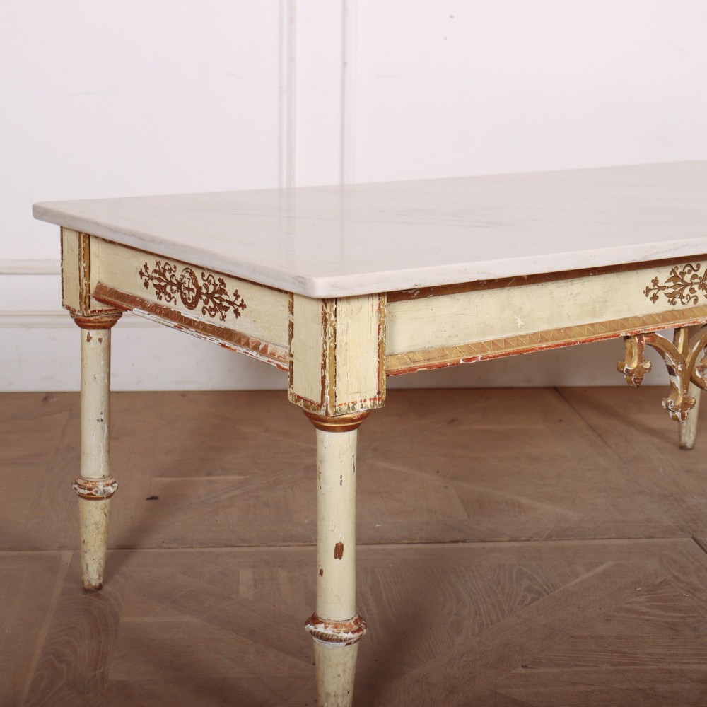 An Italian Neoclassical low coffee table featuring a flat white marble top, a cream painted apron with carved gilded accents, and tapered legs. View II