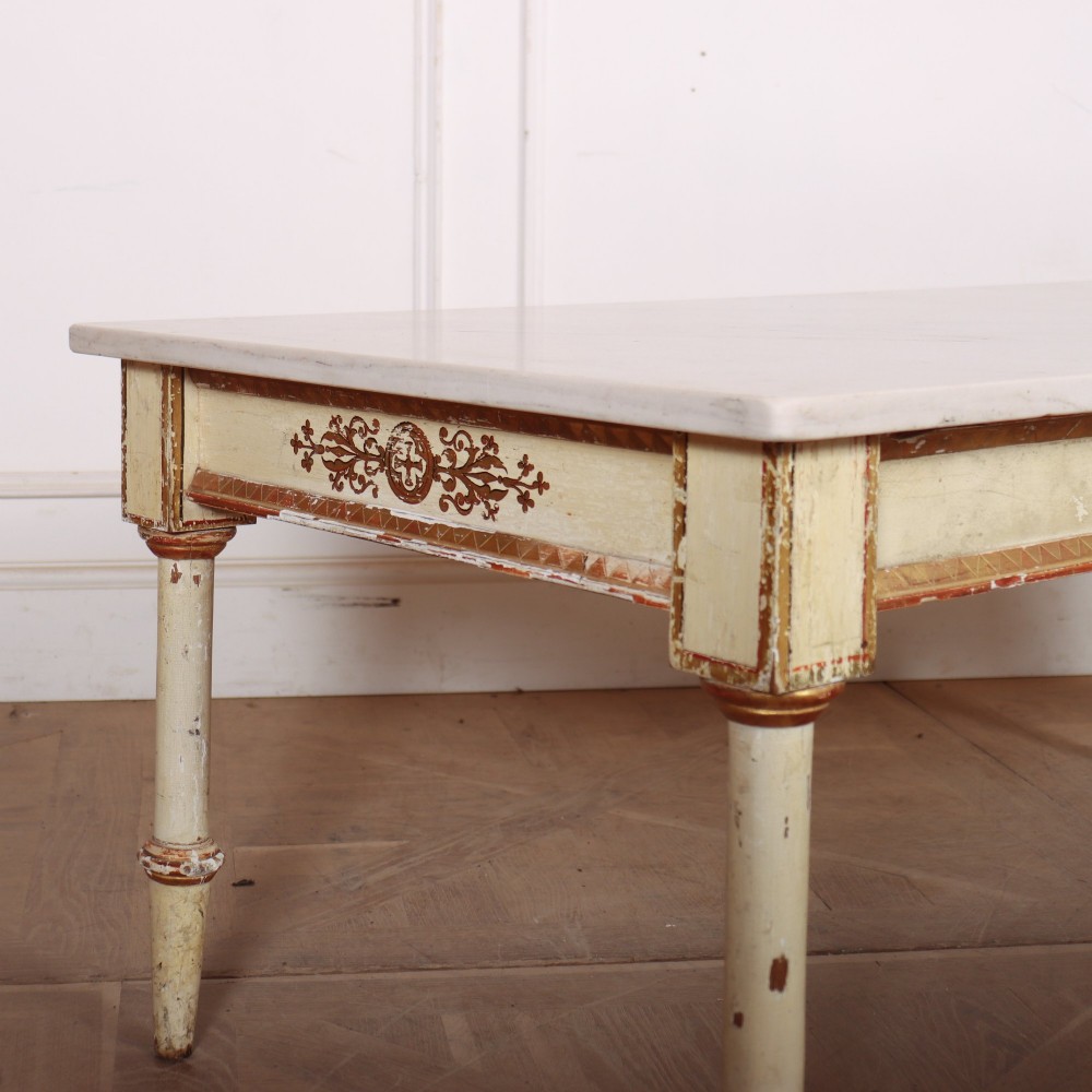 An Italian Neoclassical low coffee table featuring a flat white marble top, a cream painted apron with carved gilded accents, and tapered legs. View III