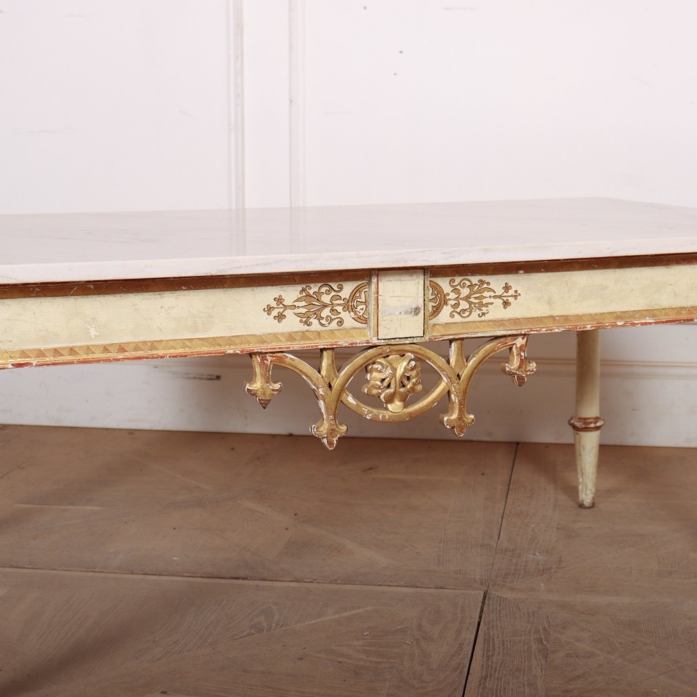 An Italian Neoclassical low coffee table featuring a flat white marble top, a cream painted apron with carved gilded accents, and tapered legs. View IV