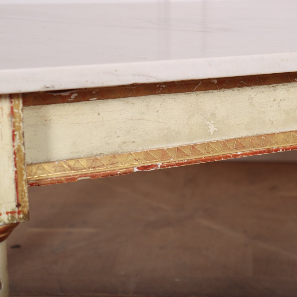 An Italian Neoclassical low coffee table featuring a flat white marble top, a cream painted apron with carved gilded accents, and tapered legs. View V