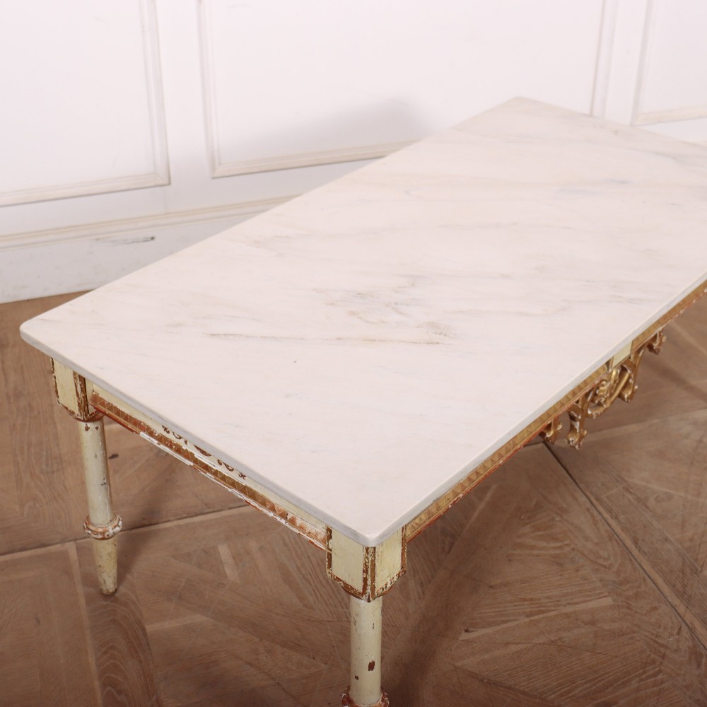 An Italian Neoclassical low coffee table featuring a flat white marble top, a cream painted apron with carved gilded accents, and tapered legs. View VI