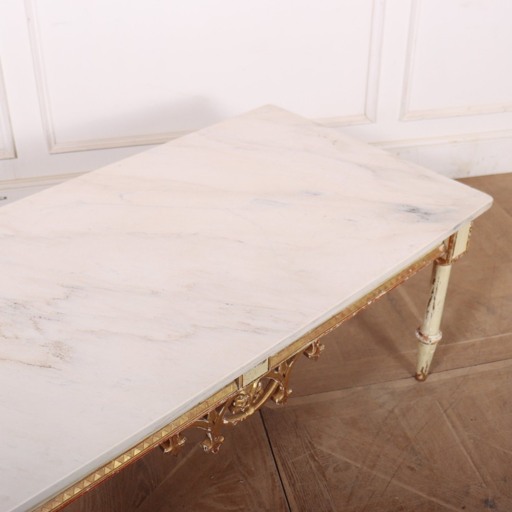 An Italian Neoclassical low coffee table featuring a flat white marble top, a cream painted apron with carved gilded accents, and tapered legs. View VII