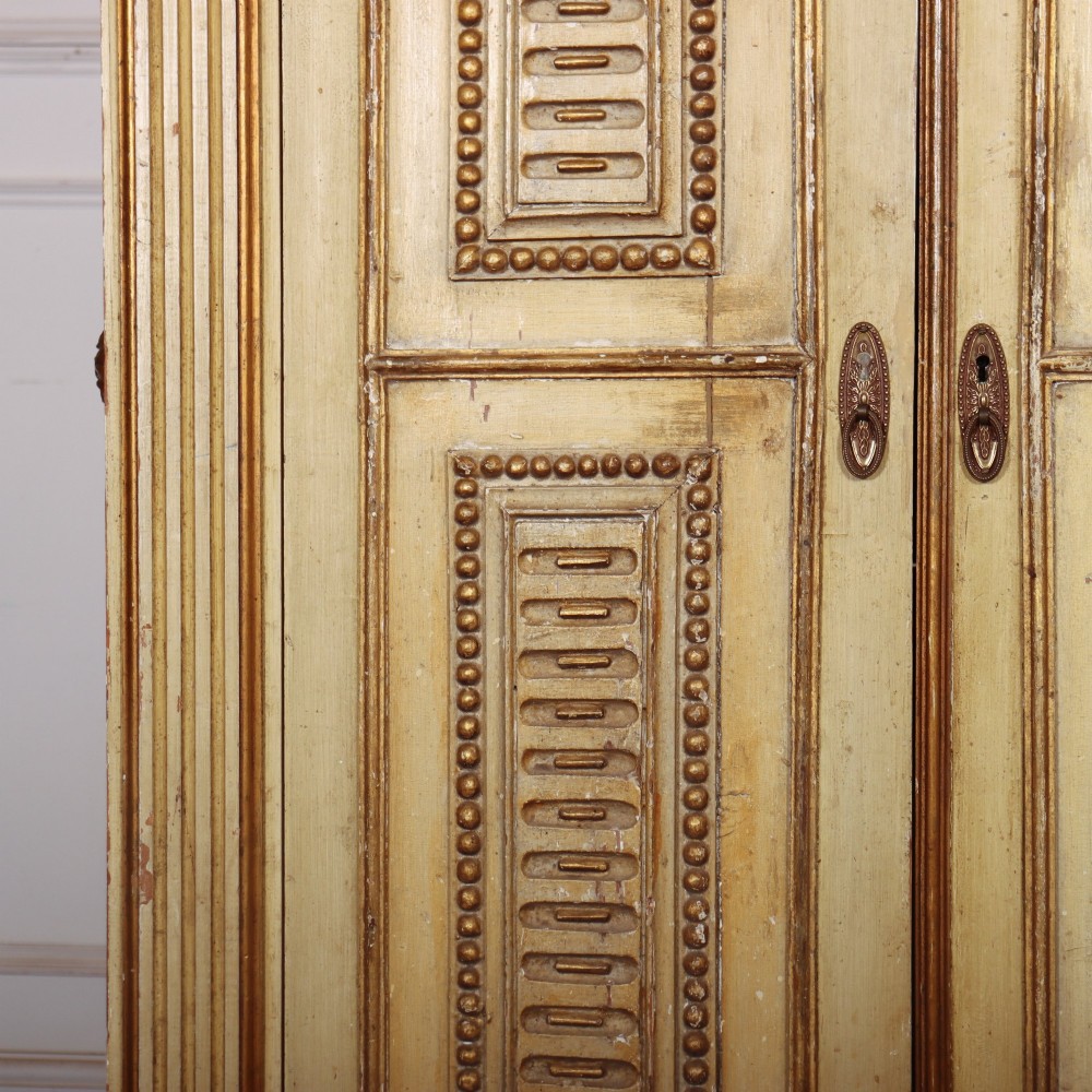 A late nineteenth-century Italian painted and gilded wooden cupboard featuring two tall doors with decorative carved panels, flanked by fluted pilasters on bun feet. View VI