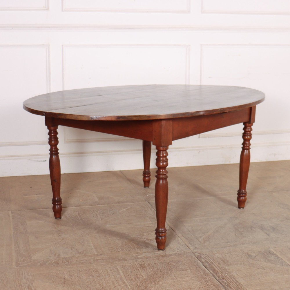 An antique French provincial dining table crafted from warm brown wood, featuring an oval top supported by four turned legs.