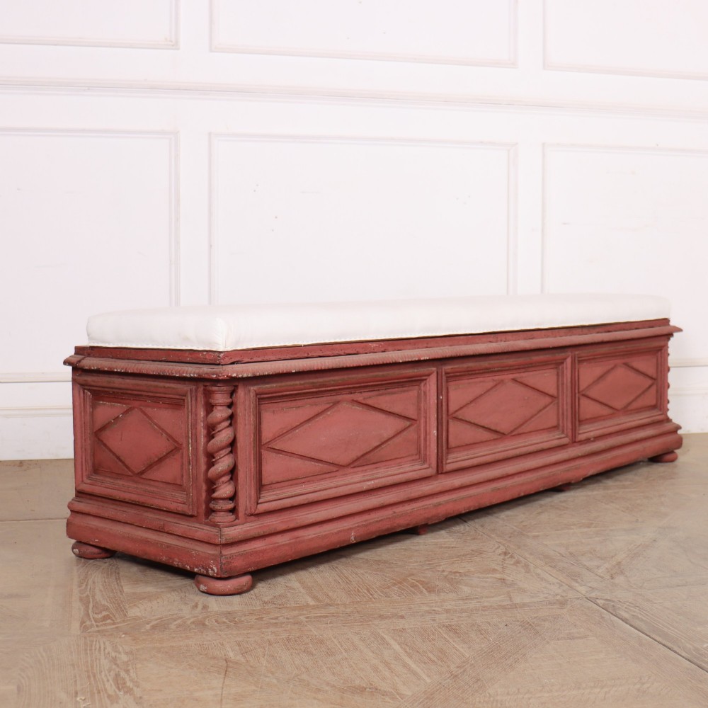 A long 19th-century Italian painted wooden bench featuring terracotta-coloured carved diamond panels, spiral corner columns, and a cream upholstered top seat cushion.