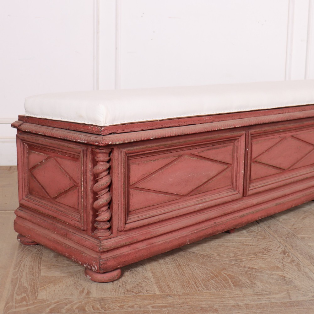 A long 19th-century Italian painted wooden bench featuring terracotta-coloured carved diamond panels, spiral corner columns, and a cream upholstered top seat cushion. View II