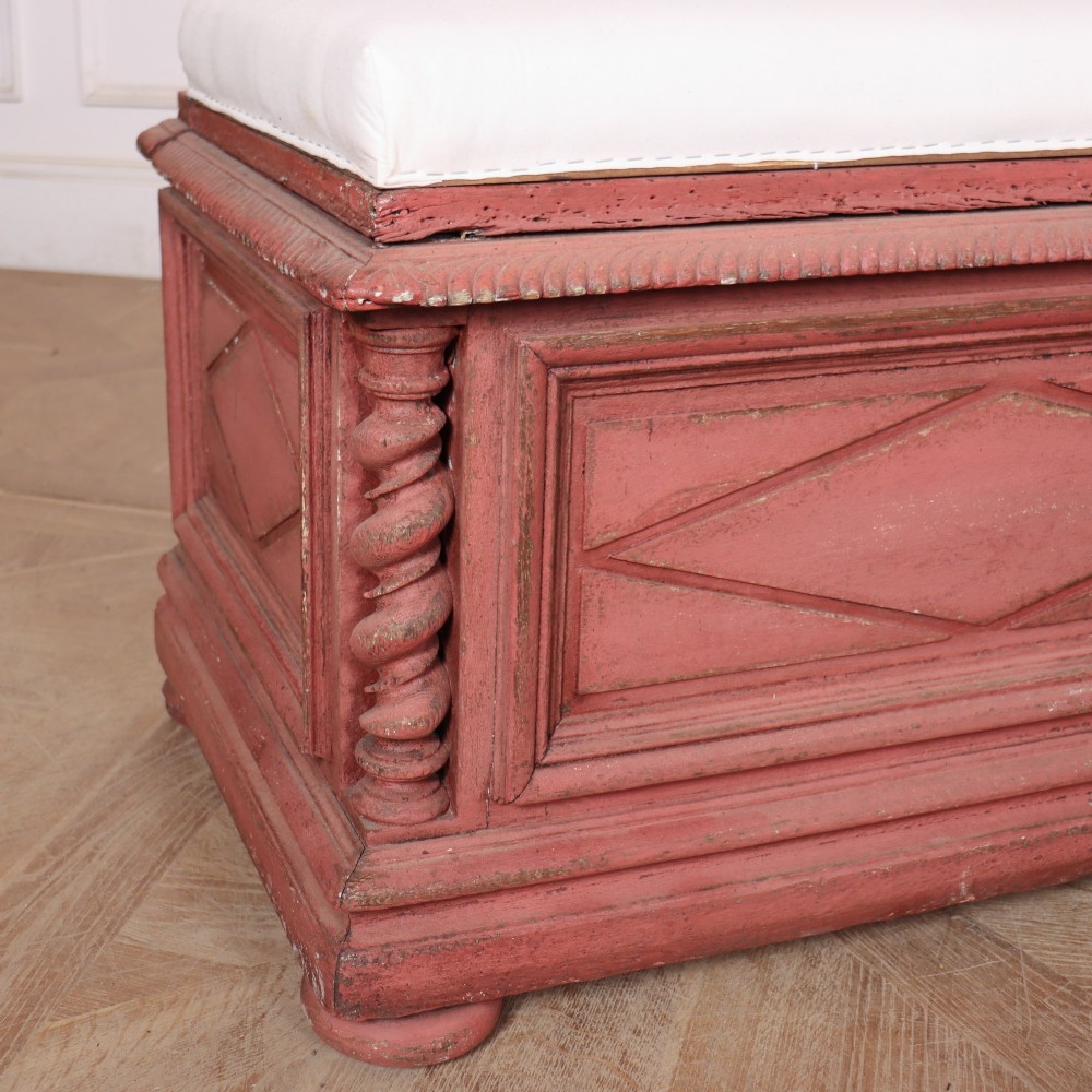 A long 19th-century Italian painted wooden bench featuring terracotta-coloured carved diamond panels, spiral corner columns, and a cream upholstered top seat cushion. View V