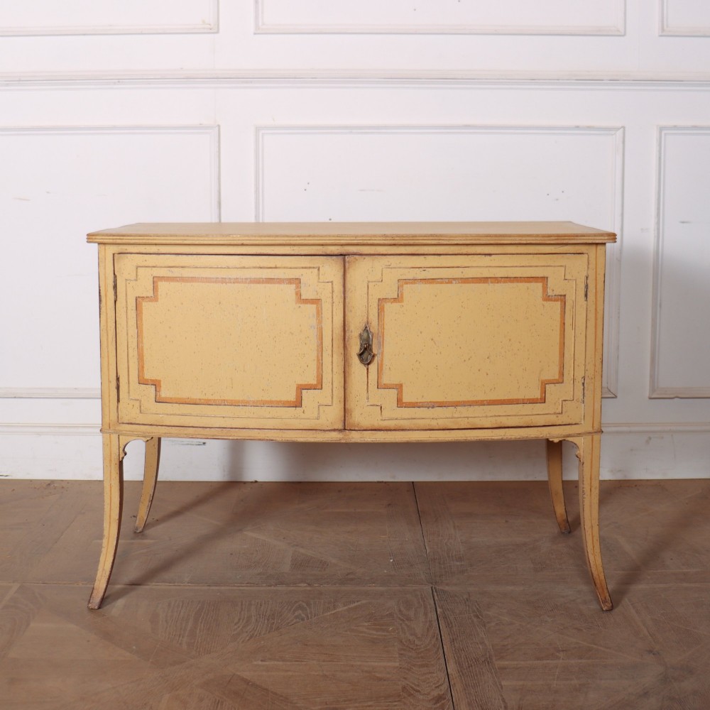 An antique English painted side cabinet in pale yellow with geometric orange door borders and tapered legs.