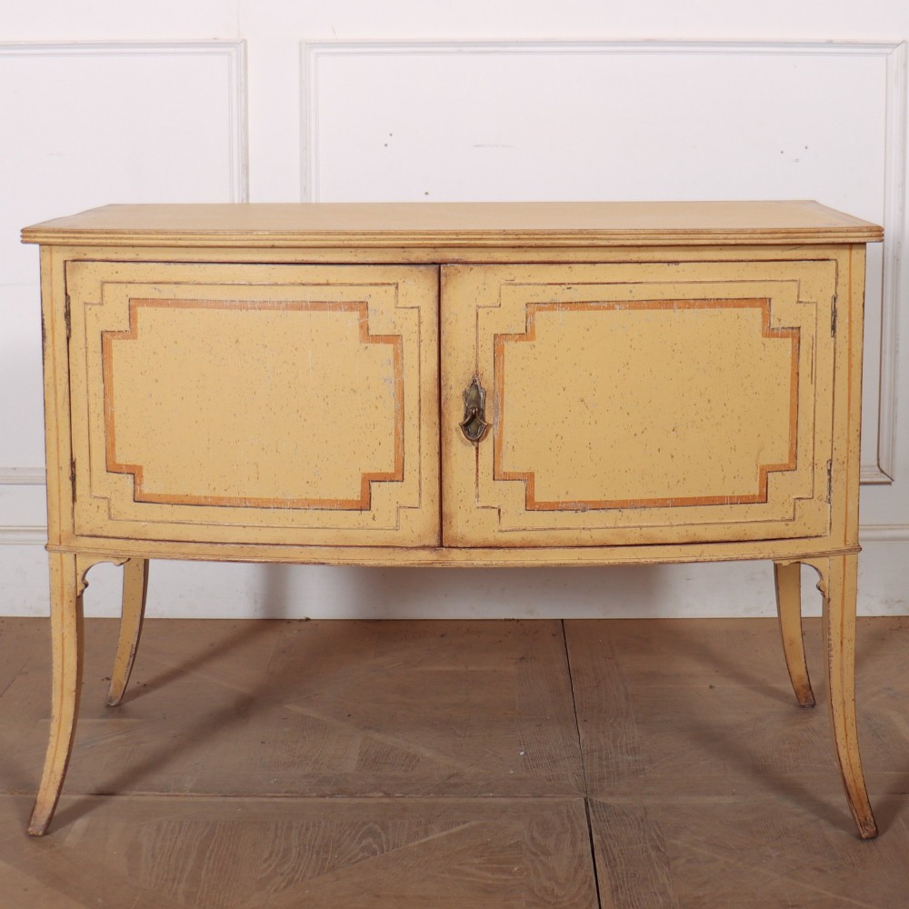 An antique English painted side cabinet in pale yellow with geometric orange door borders and tapered legs. View II