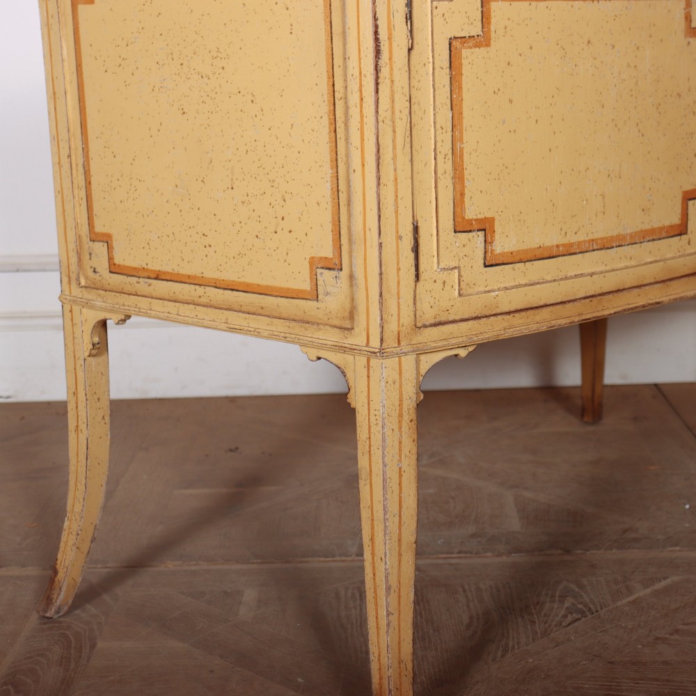 An antique English painted side cabinet in pale yellow with geometric orange door borders and tapered legs. View IX
