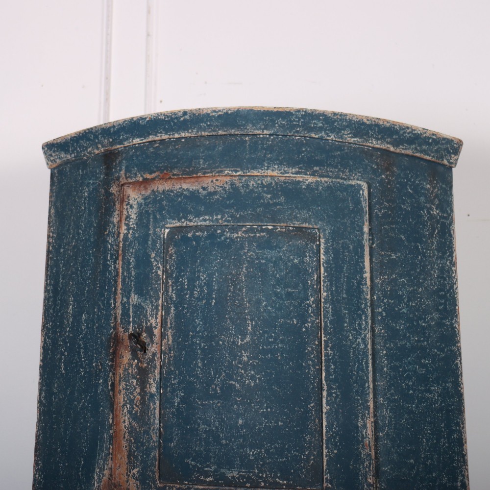 A tall Swedish bowfronted corner cupboard with a distressed blue painted finish, featuring upper and lower panel doors with an open middle shelf. View II