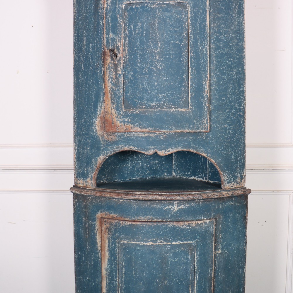 A tall Swedish bowfronted corner cupboard with a distressed blue painted finish, featuring upper and lower panel doors with an open middle shelf. View IV