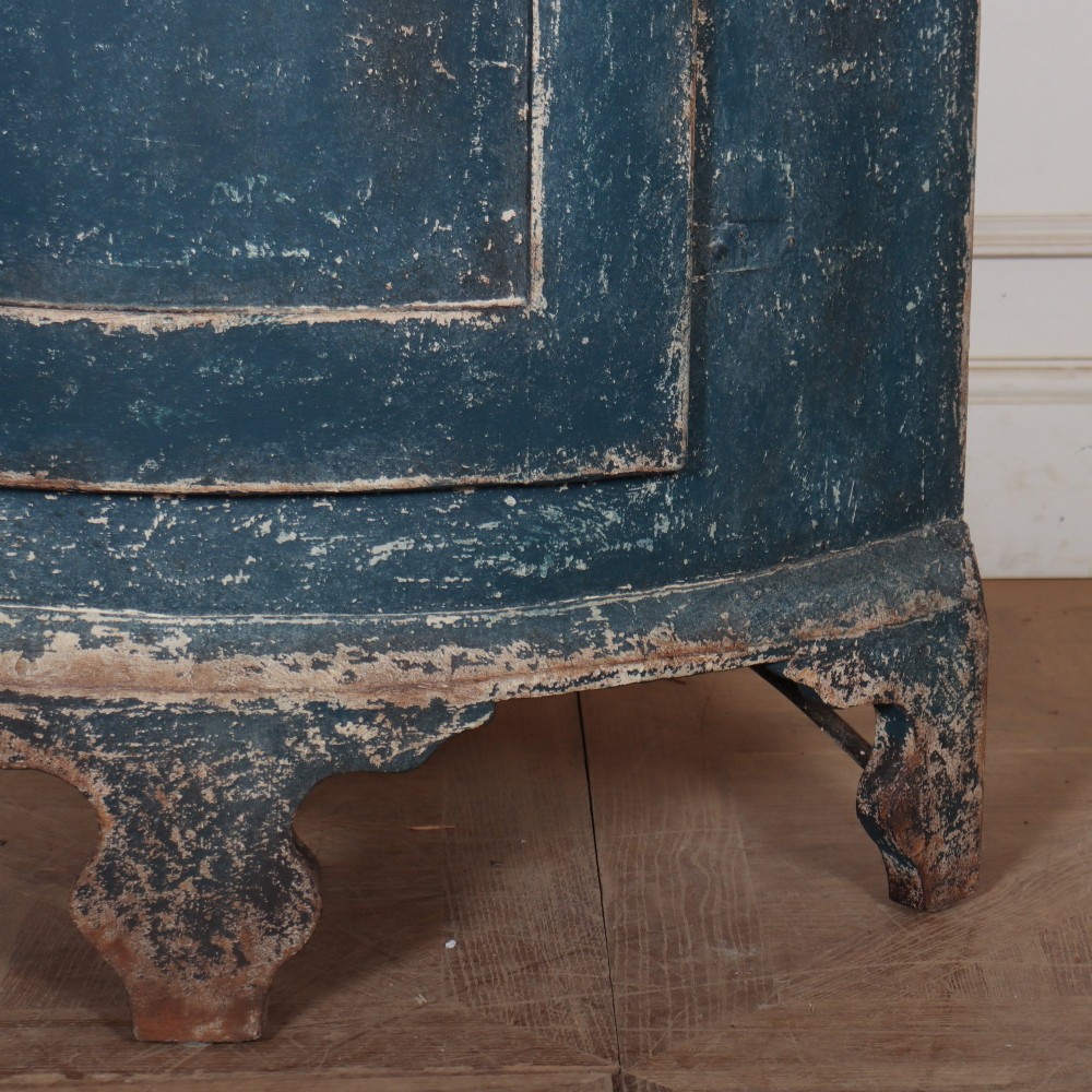 A tall Swedish bowfronted corner cupboard with a distressed blue painted finish, featuring upper and lower panel doors with an open middle shelf. View VI