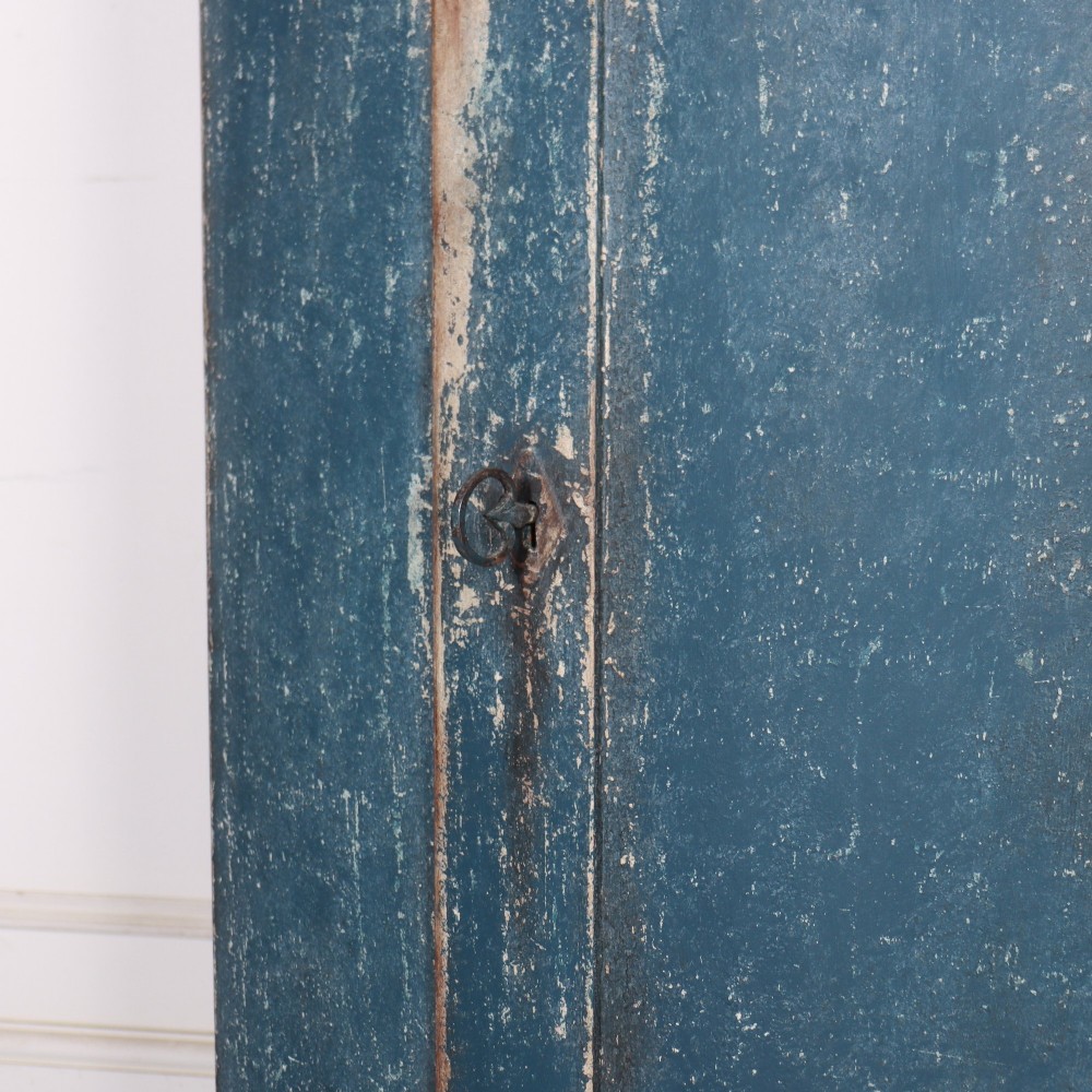 A tall Swedish bowfronted corner cupboard with a distressed blue painted finish, featuring upper and lower panel doors with an open middle shelf. View VIII