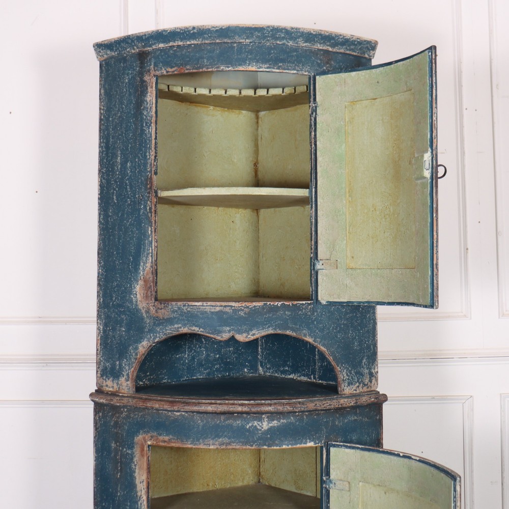 A tall Swedish bowfronted corner cupboard with a distressed blue painted finish, featuring upper and lower panel doors with an open middle shelf. View IX