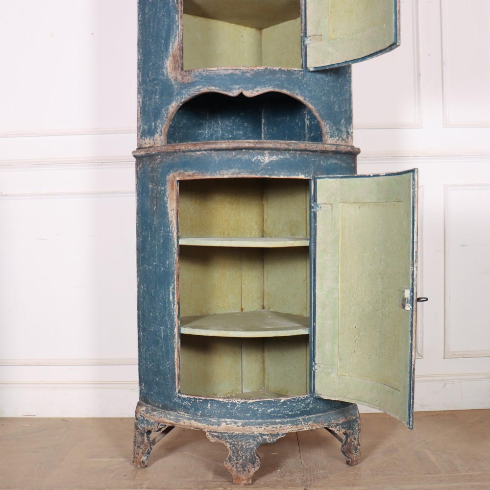 A tall Swedish bowfronted corner cupboard with a distressed blue painted finish, featuring upper and lower panel doors with an open middle shelf. View X