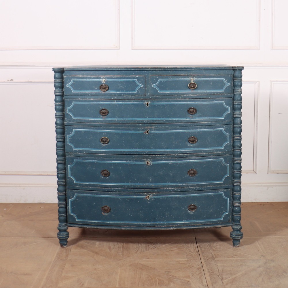 An antique English bowfront chest of drawers with a distressed blue painted finish, painted line borders, and bobbin-turned columns.