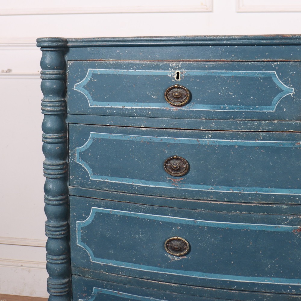 An antique English bowfront chest of drawers with a distressed blue painted finish, painted line borders, and bobbin-turned columns. View II
