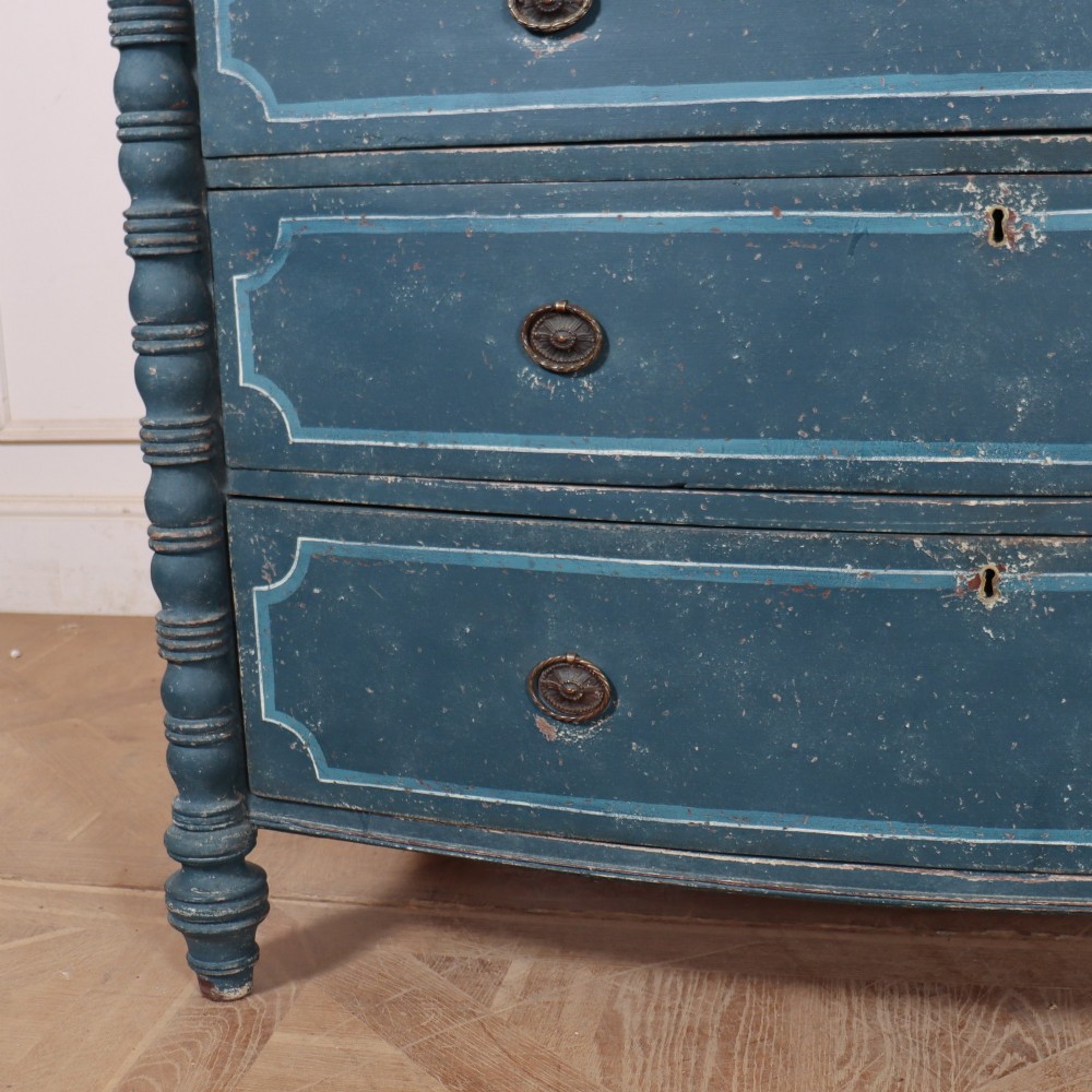 An antique English bowfront chest of drawers with a distressed blue painted finish, painted line borders, and bobbin-turned columns. View III