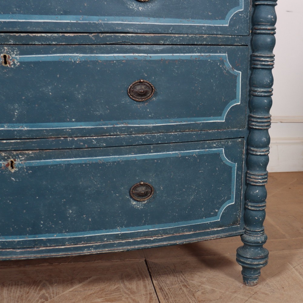 An antique English bowfront chest of drawers with a distressed blue painted finish, painted line borders, and bobbin-turned columns. View IV