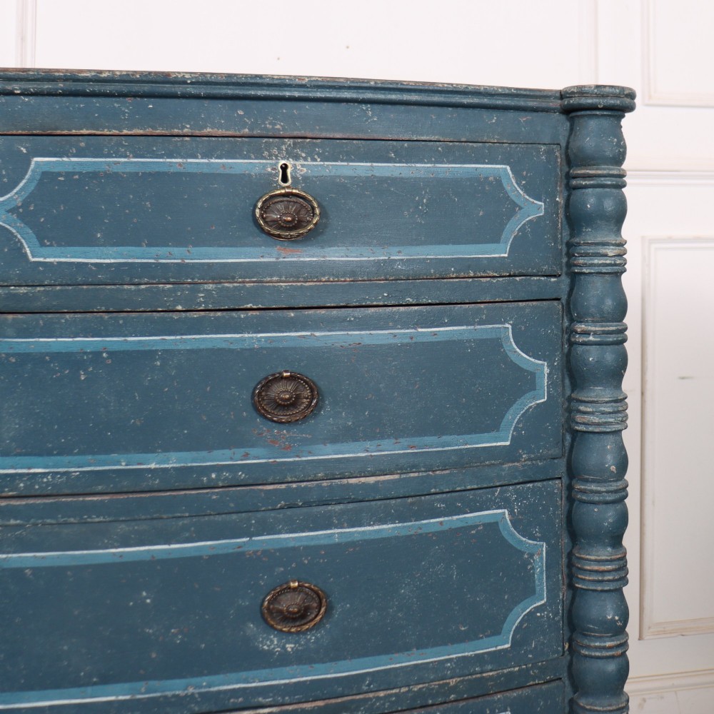 An antique English bowfront chest of drawers with a distressed blue painted finish, painted line borders, and bobbin-turned columns. View V