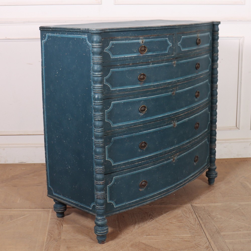 An antique English bowfront chest of drawers with a distressed blue painted finish, painted line borders, and bobbin-turned columns. View VII