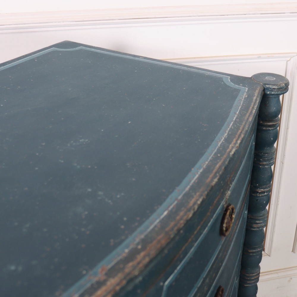 An antique English bowfront chest of drawers with a distressed blue painted finish, painted line borders, and bobbin-turned columns. View X