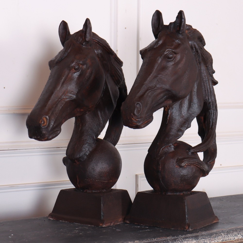A pair of dark brown cast iron horse head sculptures mounted on spherical supports with square plinth bases.