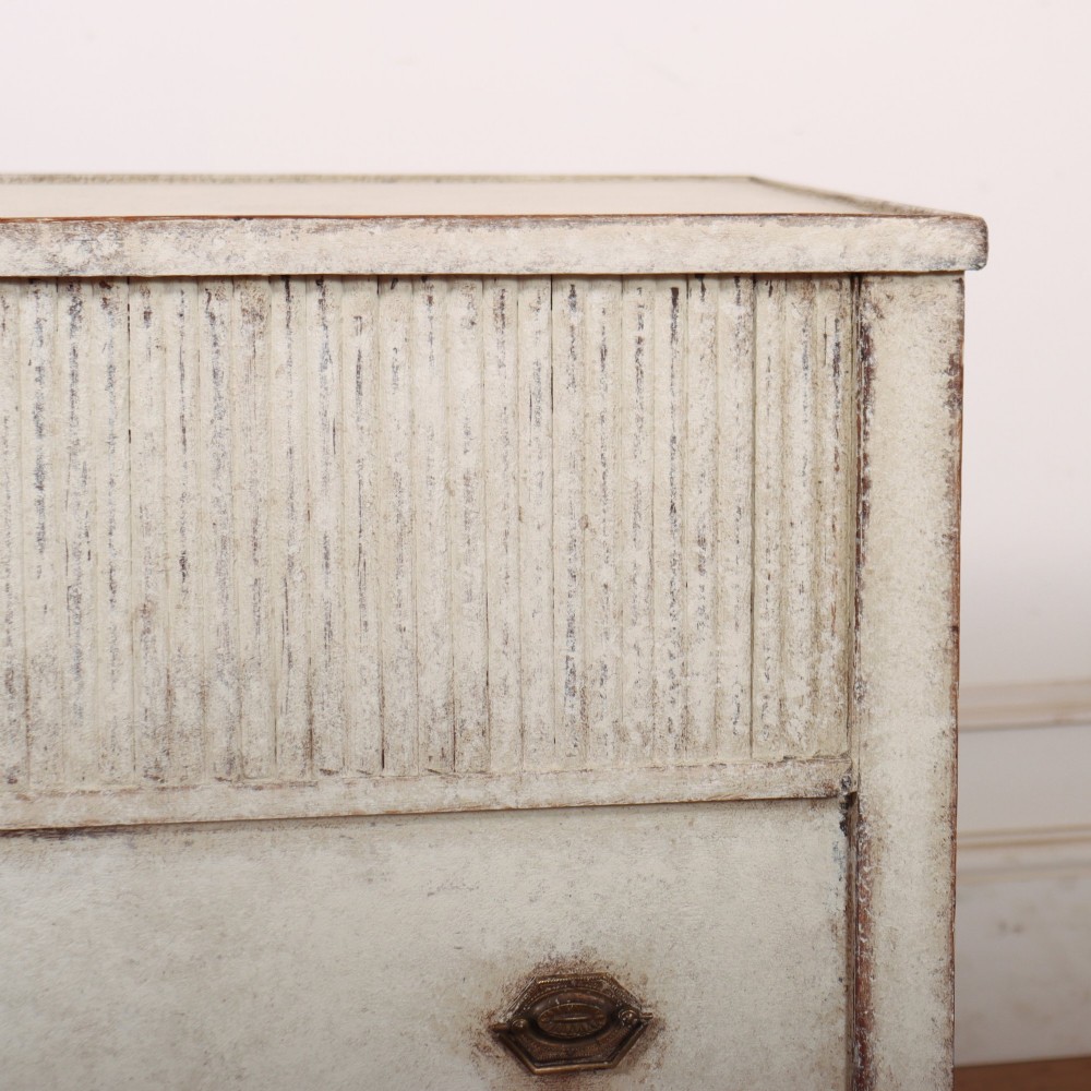 An antique cream painted Dutch bedside cabinet featuring a fluted upper section, a lower drawer with brass handles, and square tapered legs. View III