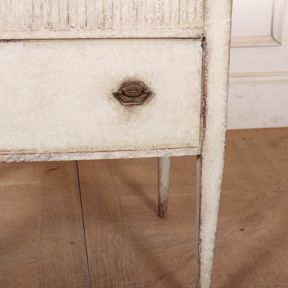 An antique cream painted Dutch bedside cabinet featuring a fluted upper section, a lower drawer with brass handles, and square tapered legs. View IV