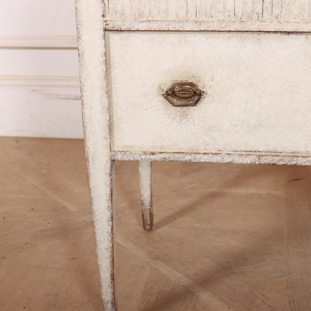 An antique cream painted Dutch bedside cabinet featuring a fluted upper section, a lower drawer with brass handles, and square tapered legs. View V