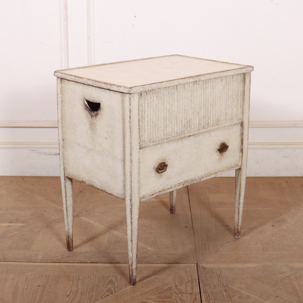 An antique cream painted Dutch bedside cabinet featuring a fluted upper section, a lower drawer with brass handles, and square tapered legs. View VI