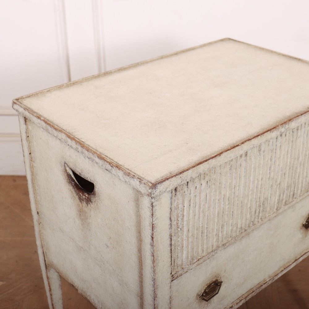 An antique cream painted Dutch bedside cabinet featuring a fluted upper section, a lower drawer with brass handles, and square tapered legs. View VII