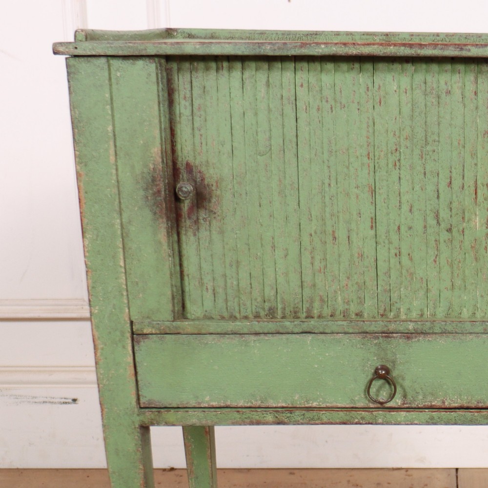 A Dutch provincial green painted bedside table with a slatted tambour door, lower drawer, and tapered square legs. View IV