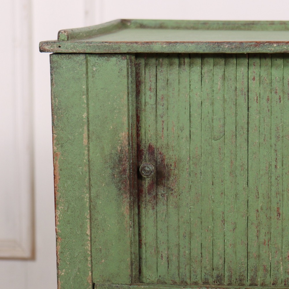 A Dutch provincial green painted bedside table with a slatted tambour door, lower drawer, and tapered square legs. View VII