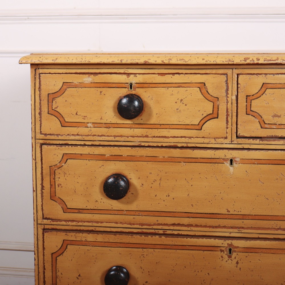 An antique yellow painted pine chest of drawers with two small drawers over three full-width drawers, featuring dark line border detailing, timber knobs, and turned feet. View II