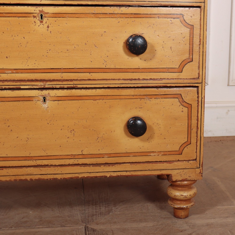 An antique yellow painted pine chest of drawers with two small drawers over three full-width drawers, featuring dark line border detailing, timber knobs, and turned feet. View IV