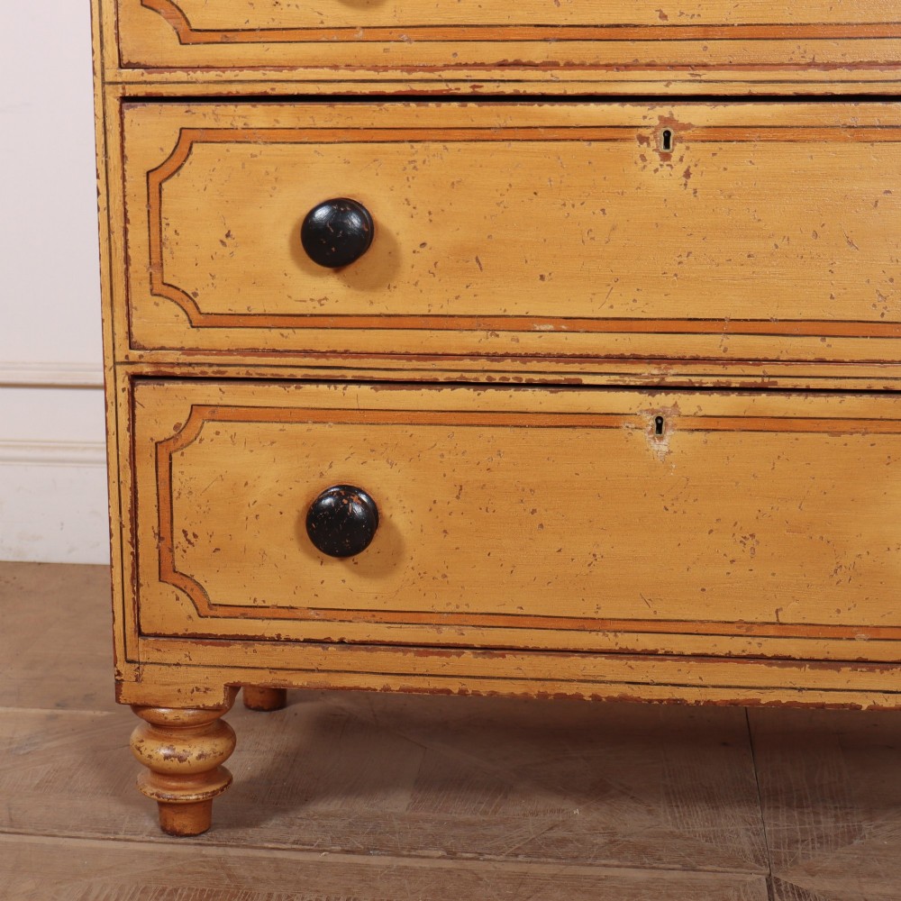 An antique yellow painted pine chest of drawers with two small drawers over three full-width drawers, featuring dark line border detailing, timber knobs, and turned feet. View V