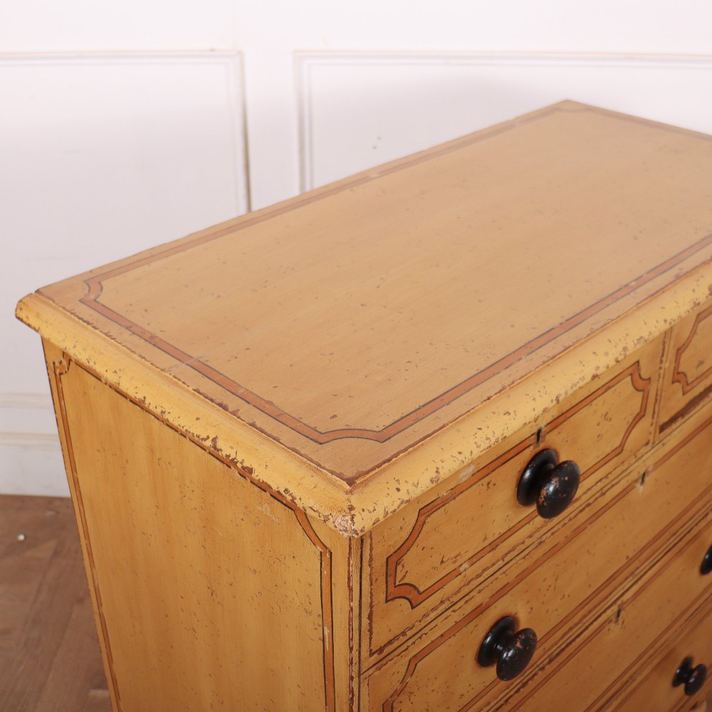 An antique yellow painted pine chest of drawers with two small drawers over three full-width drawers, featuring dark line border detailing, timber knobs, and turned feet. View X