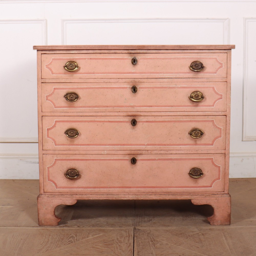 An antique English four-drawer chest featuring a muted pink painted finish with contrasting painted frame borders and brass oval handles on bracket feet.
