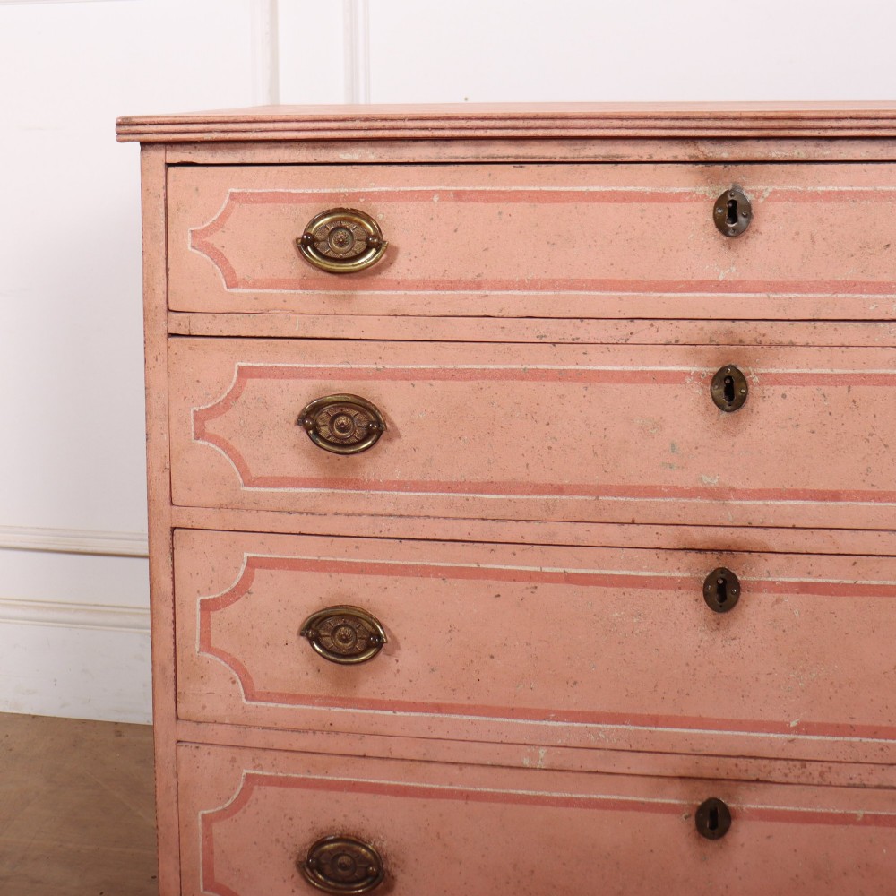 An antique English four-drawer chest featuring a muted pink painted finish with contrasting painted frame borders and brass oval handles on bracket feet. View II