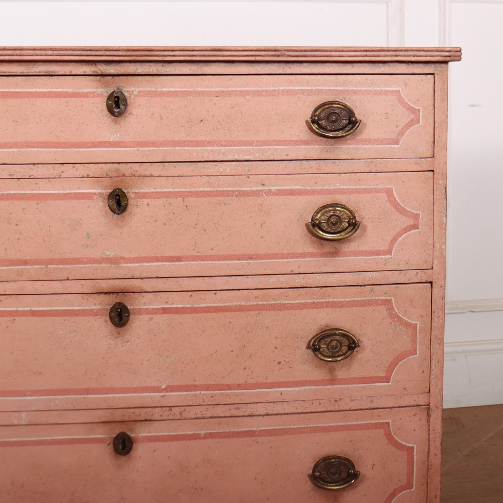 An antique English four-drawer chest featuring a muted pink painted finish with contrasting painted frame borders and brass oval handles on bracket feet. View III