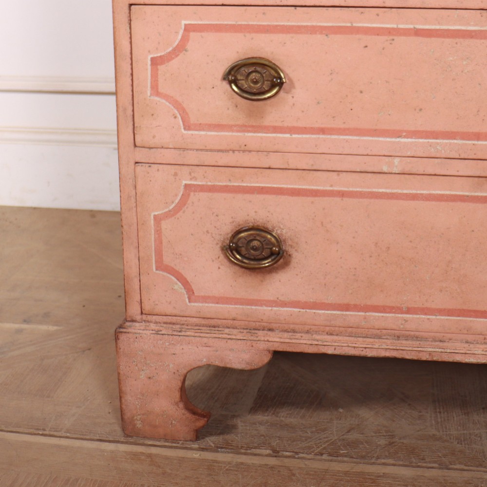 An antique English four-drawer chest featuring a muted pink painted finish with contrasting painted frame borders and brass oval handles on bracket feet. View IV