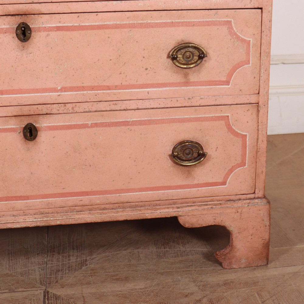 An antique English four-drawer chest featuring a muted pink painted finish with contrasting painted frame borders and brass oval handles on bracket feet. View V