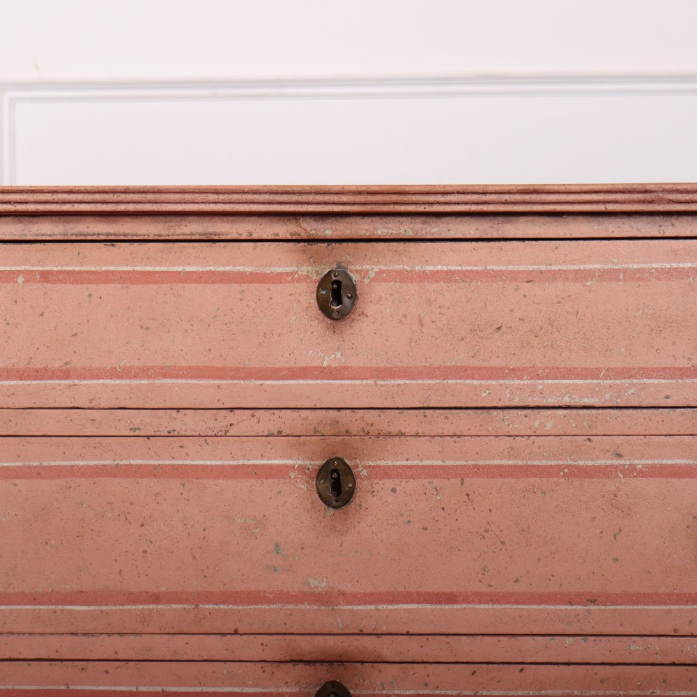 An antique English four-drawer chest featuring a muted pink painted finish with contrasting painted frame borders and brass oval handles on bracket feet. View VI